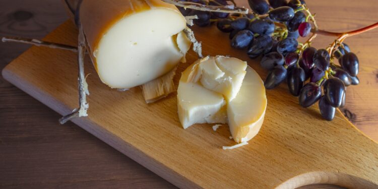 Traditional Greek smoked cheese Metsovone on a wooden board with grapes from the village Metsovo in Greece