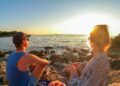 Sithonia - Rear view of happy couple admiring the sunset on a remote pebble beach on the peninsula of Sithonia, Greece