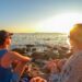 Sithonia - Rear view of happy couple admiring the sunset on a remote pebble beach on the peninsula of Sithonia, Greece